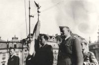 Slavnostní leteckou standartu drží zbrojíř 311. československé bombardovací perutě Viktor Kropš. (Jeho osud by rovněž vydal na knihu zejména svými dramaty po roce 1948. Jeho letka byla v roce 1946 převelena na letiště Plzeň-Bory. Při přehlídce uskutečněné právě v Plzni v roce 1945 se seznámil se svou budoucí chotí Jiřinou. Po únoru 1948 se spolu s ní za pomoci převaděče pokusili jedné noci projít domažlickými lesy za hranice, avšak byli zadrženi. Viktor i Jiřina se na pohraničníky vrhli, strhla se rvačka a Viktor chtěl použít i svůj revolver. Nicméně pohraničníci byli v přesile. Jiřina skončila na rok v ženské káznici a Viktor po dlouhém věznění s trýznivými výslechy nakonec v jáchymovských dolech, což mu natrvalo podlomilo zdraví. I této rodině se Jan v nejtěžších dobách snažil pomáhat a přátelské vazby se upevnily až do „rodinného“ pouta. Když Viktor po propuštění po několika málo letech na svobodě na následky věznění zemřel, byl Jan požádán, aby vyprovodil jejich dceru Šárku jako „druhý táta“ k oltáři, a naproti tomu Jiřinka „dělala druhou mámu“ Ivetě až do své smrti v roce 2014.)